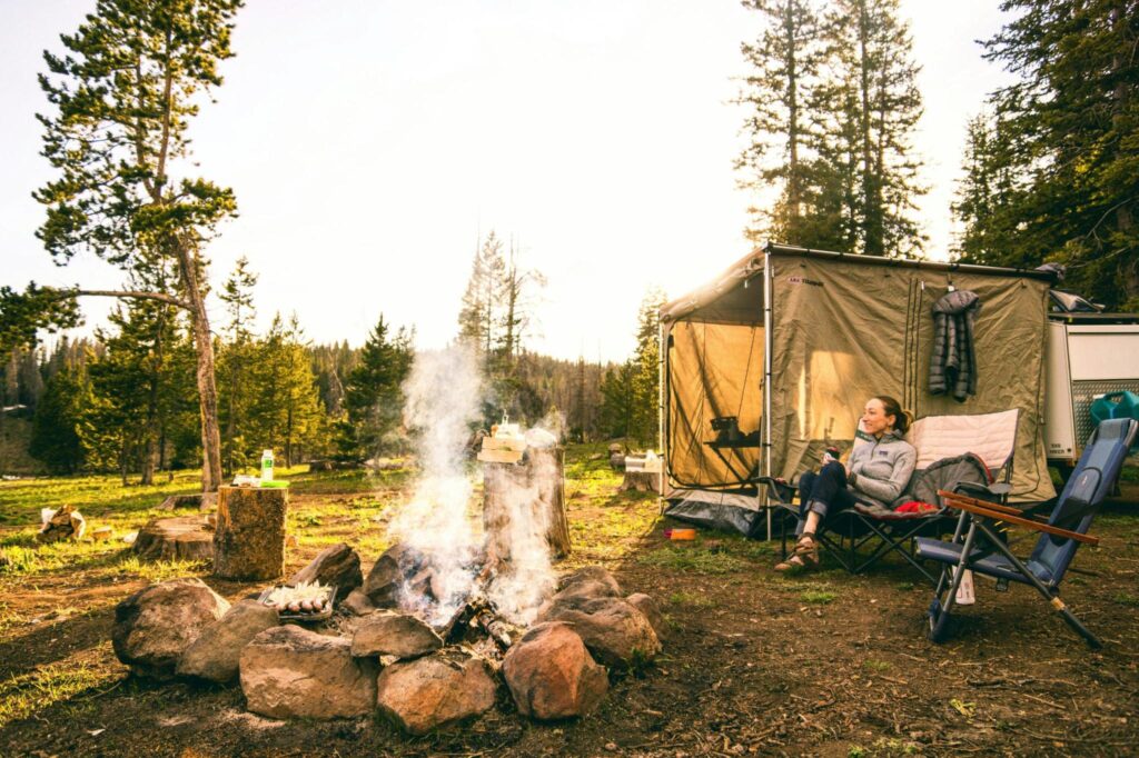 Campsite with tent, fire, and woman in chair in front of fire